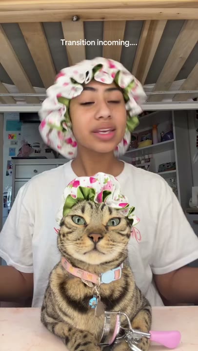 Frame at 0 seconds: Creator and foreground cat appear in matching floral bonnets beneath the transition teaser.
