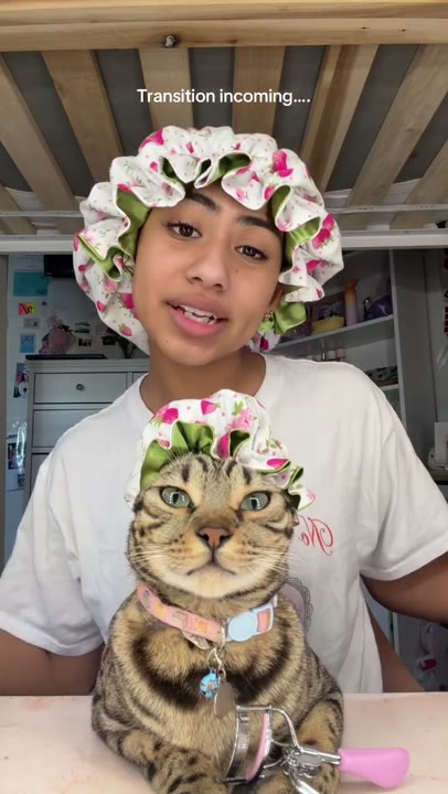 Frame at 1 seconds: Creator and foreground cat appear in matching floral bonnets beneath the transition teaser.